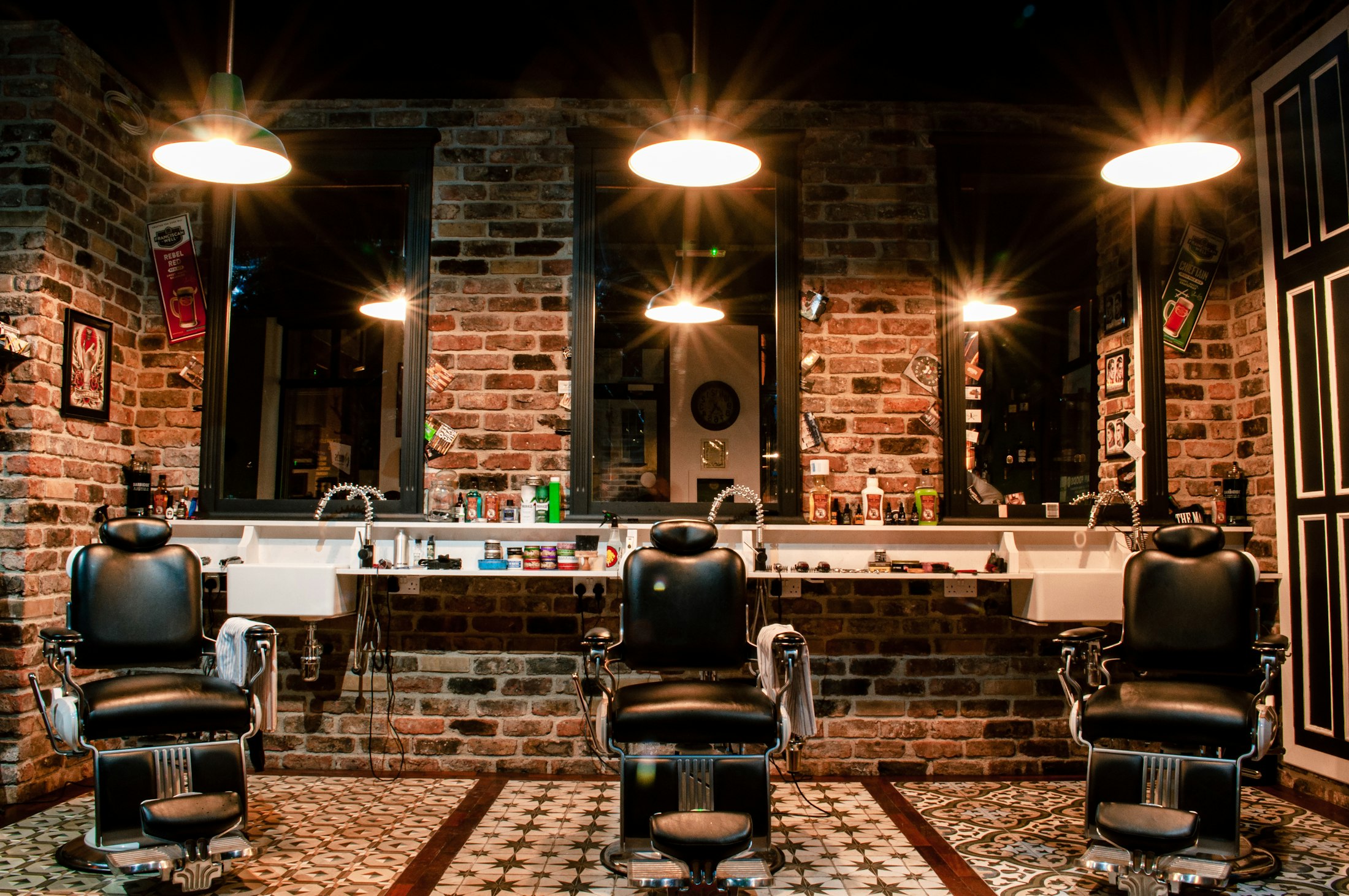 Barber shop interior with brick walls, pendant lights, mirrors and black leather chairs