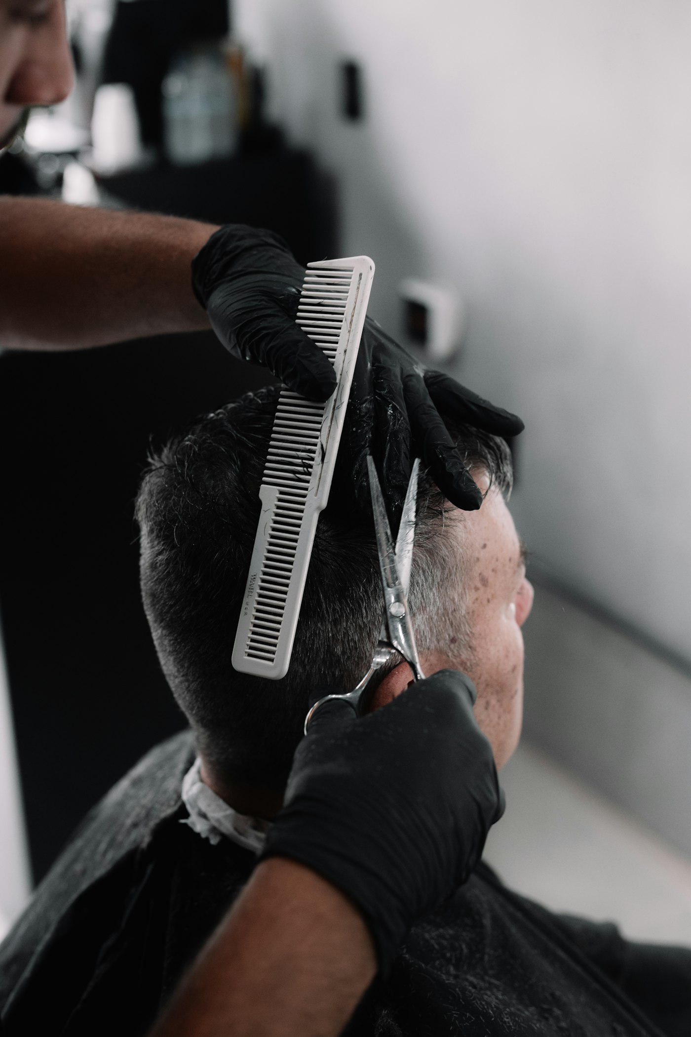 Barber in black gloves cutting hair with scissors over a comb